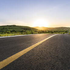 Curved mountain road with sunsetting in the background.
