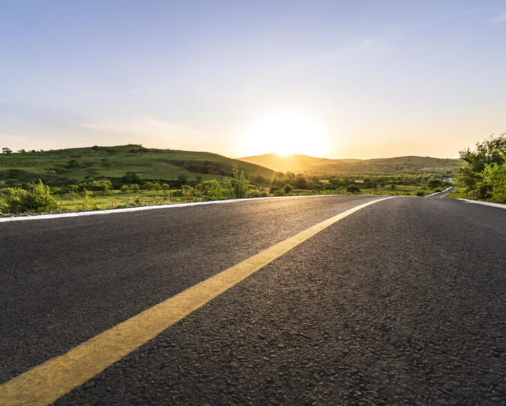 Curved mountain road with sunsetting in the background.